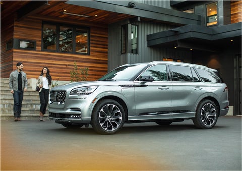 A couple approach a 2023 Lincoln Aviator® Grand Touring model parked in the driveway of a modern home