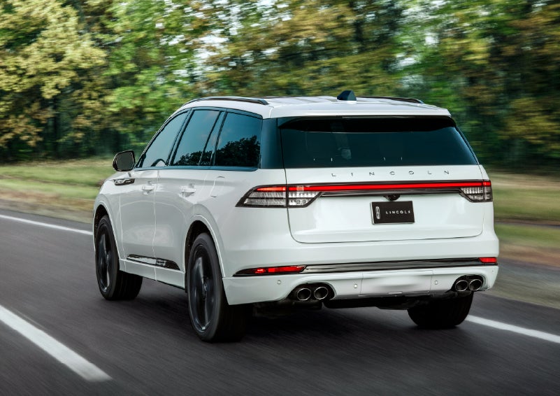 A white 2026 Lincoln Aviator® SUV is being driven away down a road lined with colorful trees. | Mike Carpino Lincoln in Pittsburg KS