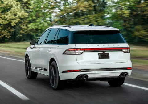 A white 2026 Lincoln Aviator® SUV is being driven away down a road lined with colorful trees. | Mike Carpino Lincoln in Pittsburg KS