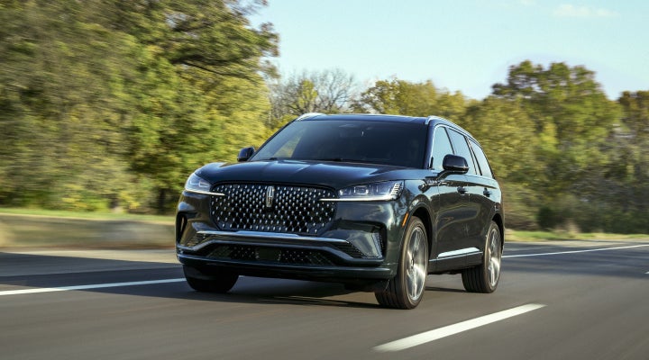 A 2026 Lincoln Black Label™ Aviator® SUV is being driven down a road lined with trees. | Mike Carpino Lincoln in Pittsburg KS
