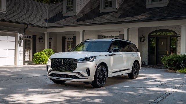 A white 2026 Lincoln Aviator® SUV is parked in the driveway of a luxury home. | Mike Carpino Lincoln in Pittsburg KS
