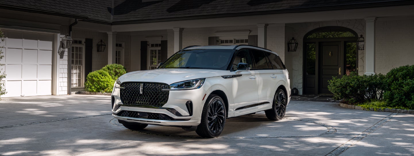 A white 2026 Lincoln Aviator® SUV is parked in the driveway of a luxury home. | Mike Carpino Lincoln in Pittsburg KS