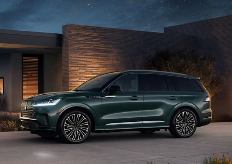 A green 2027 Lincoln Aviator® SUV is parked outside a contemporary home. | Mike Carpino Lincoln in Pittsburg KS