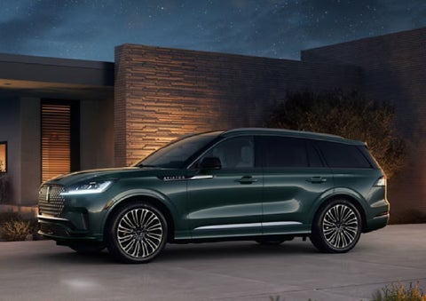 A green 2027 Lincoln Aviator® SUV is parked outside a contemporary home. | Mike Carpino Lincoln in Pittsburg KS