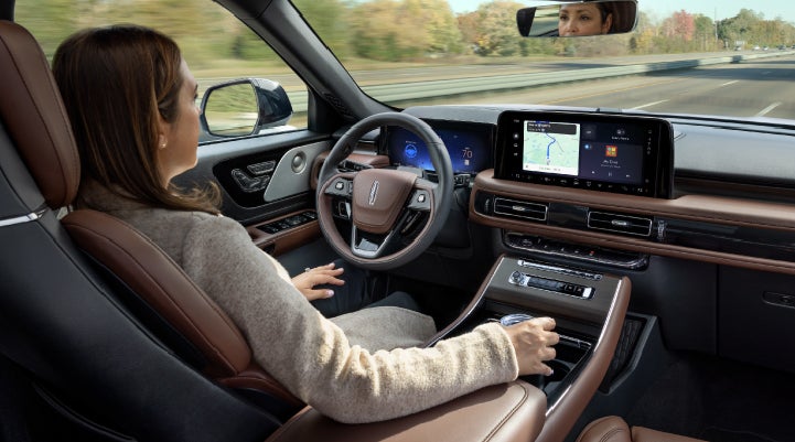 A 2027 Lincoln Aviator® SUV is being driven hands-free on a highway lined with trees. | Mike Carpino Lincoln in Pittsburg KS