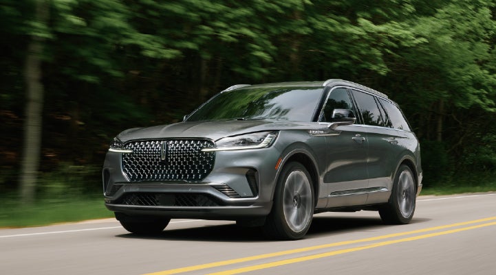 A 2027 Lincoln Aviator® SUV is being driven down a road lined with trees. | Mike Carpino Lincoln in Pittsburg KS