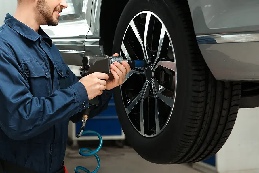Mechanic in blue jumpsuit using an impact wrench to change a tire on a lifted car