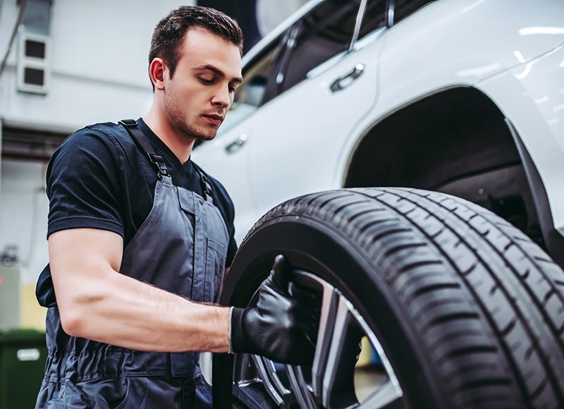 A male mechanic installs a tire on a car inside a garage.